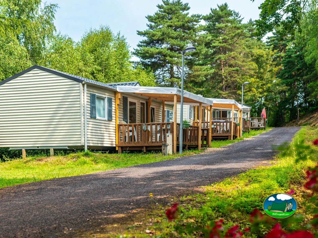 hilera de bungalows con porches de madera junto a un camino arbolado con flores rojas en primer plano