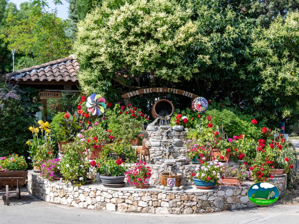 jardín decorativo con fuente de piedra, macetas de geranios y arco de bienvenida junto a la recepción en Aix-en-Provence