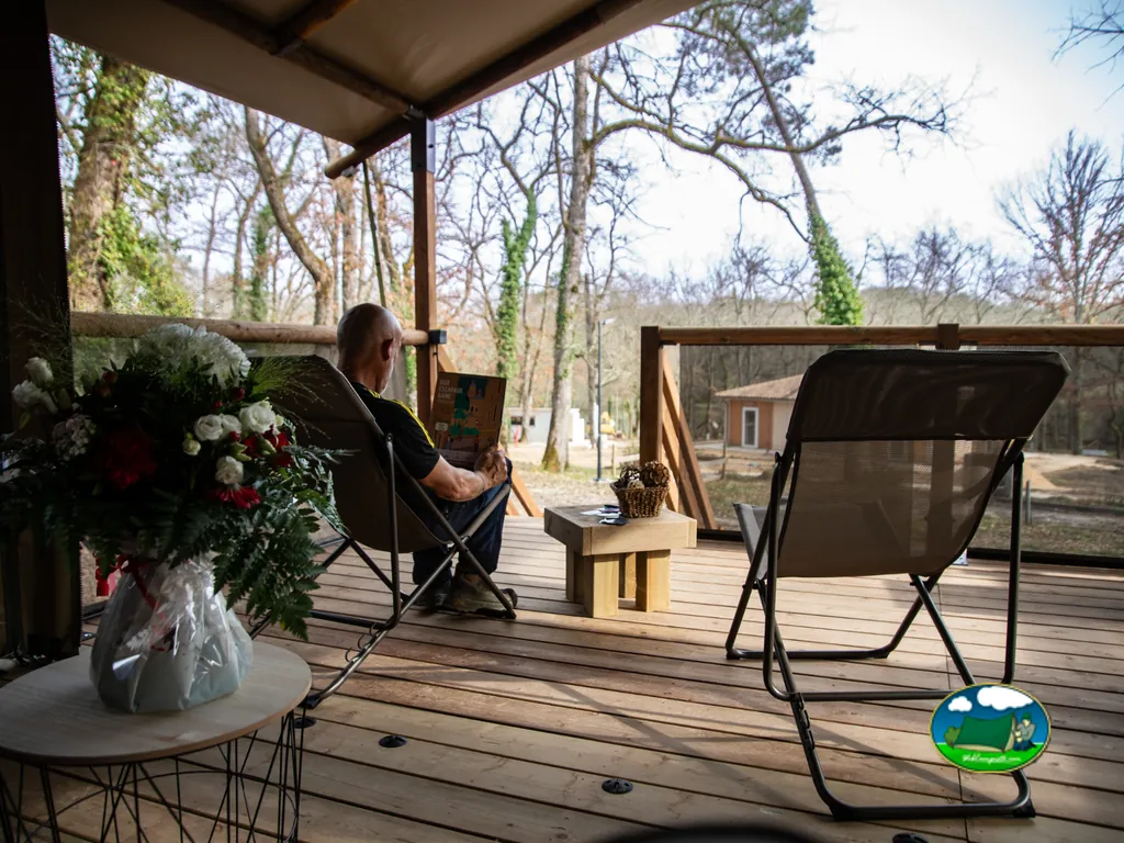 hombre sentado leyendo en la terraza de madera de un chalet entre árboles en Saint-Amand-de-Vergt