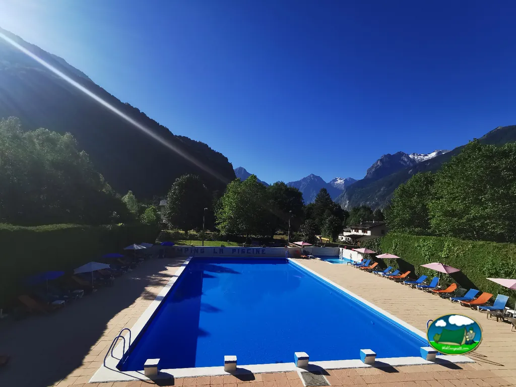 piscina azul del camping con vistas a montañas nevadas y tumbonas vacías en Le Bourg-d'Oisans