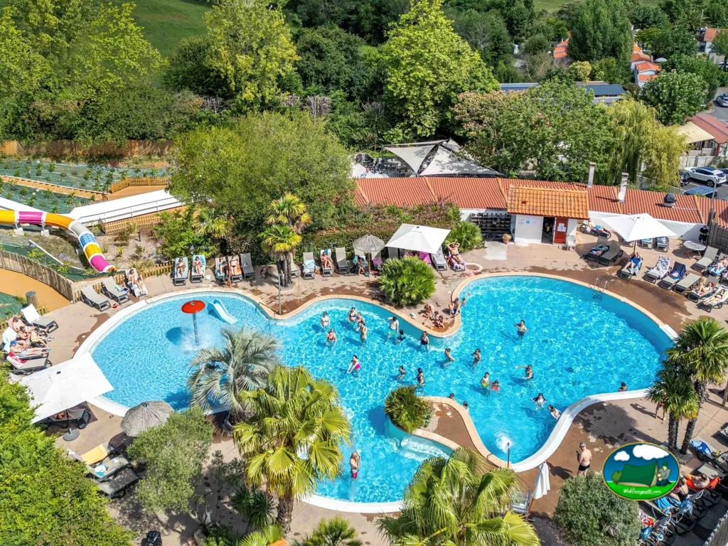 vista aérea de la piscina con tobogán y bañistas rodeada de palmeras en el camping