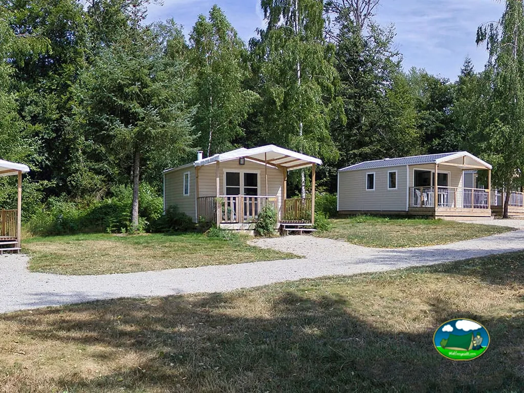 dos chalets con terraza cubierta entre árboles en el camping de Bulgnéville