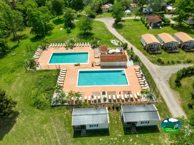 vista aérea de dos piscinas rectangulares con tumbonas y cabañas de tejado naranja en el camping de Mazères