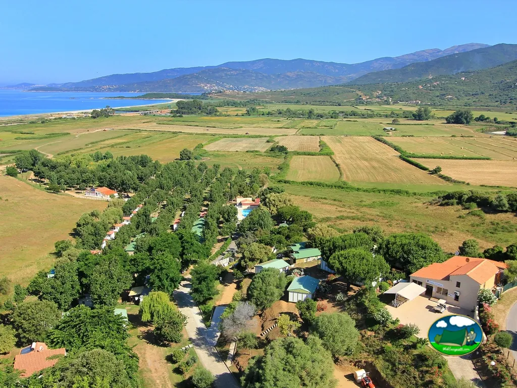 vista aérea del camping entre campos y arboledas con piscina y bungalows cerca del mar en Casaglione