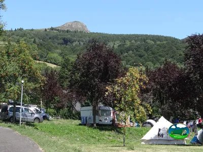 parcelas del camping con caravana y tienda de campaña bajo árboles con un puy volcánico al fondo en La Bourboule
