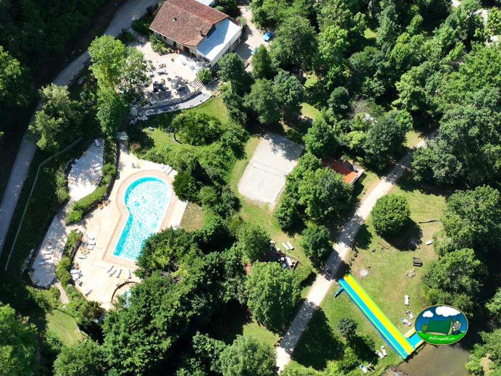 vista aérea del camping con piscina en forma de ojo de cerradura, tobogán acuático hacia el río y edificio de recepción de tejado rojo