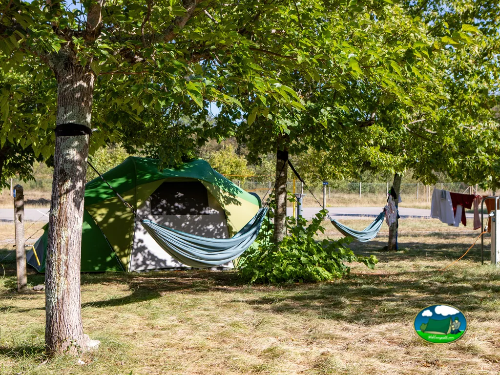 tienda de campaña con hamacas colgadas entre los árboles de la parcela y ropa tendida al fondo en el camping de Tourrettes