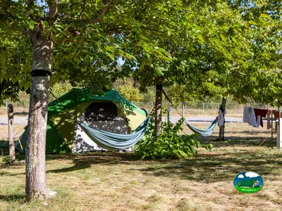 tienda de campaña con hamacas colgadas entre los árboles de la parcela y ropa tendida al fondo en el camping de Tourrettes