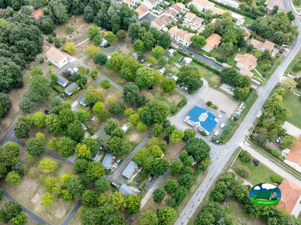 vista aérea del camping con parcelas arboladas, casas móviles y el edificio de recepción de tejado azul en Saint-Georges-de-Didonne