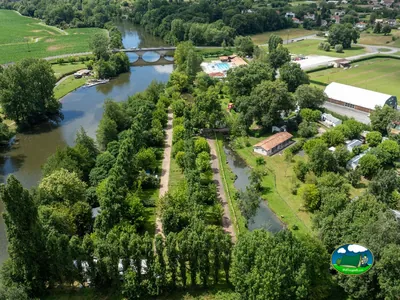 vista aérea del camping junto al río con piscina, puente de piedra y parcelas arboladas en Neuvic