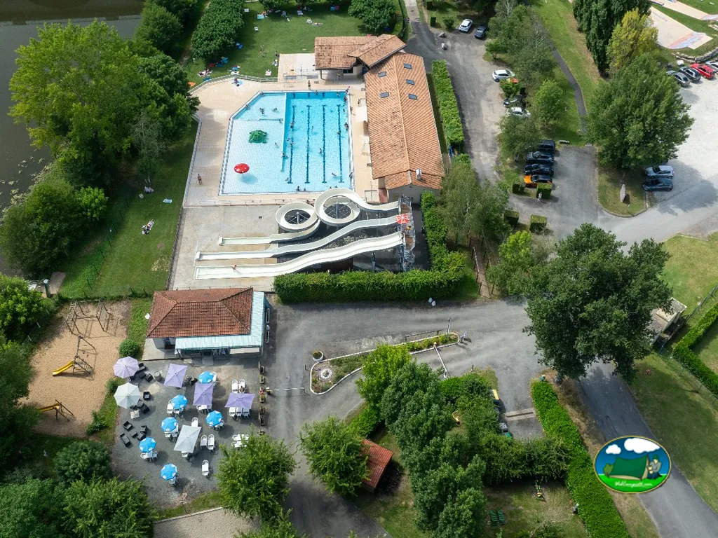 piscina del camping con toboganes en espiral, terraza con sombrillas y parque infantil vistos desde el aire, con bañistas en el agua