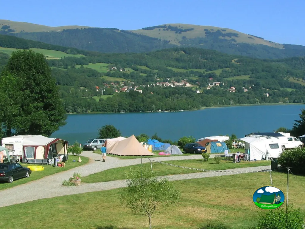 parcelas con tiendas y caravanas junto al lago de Saint-Théoffrey, con montañas boscosas al fondo