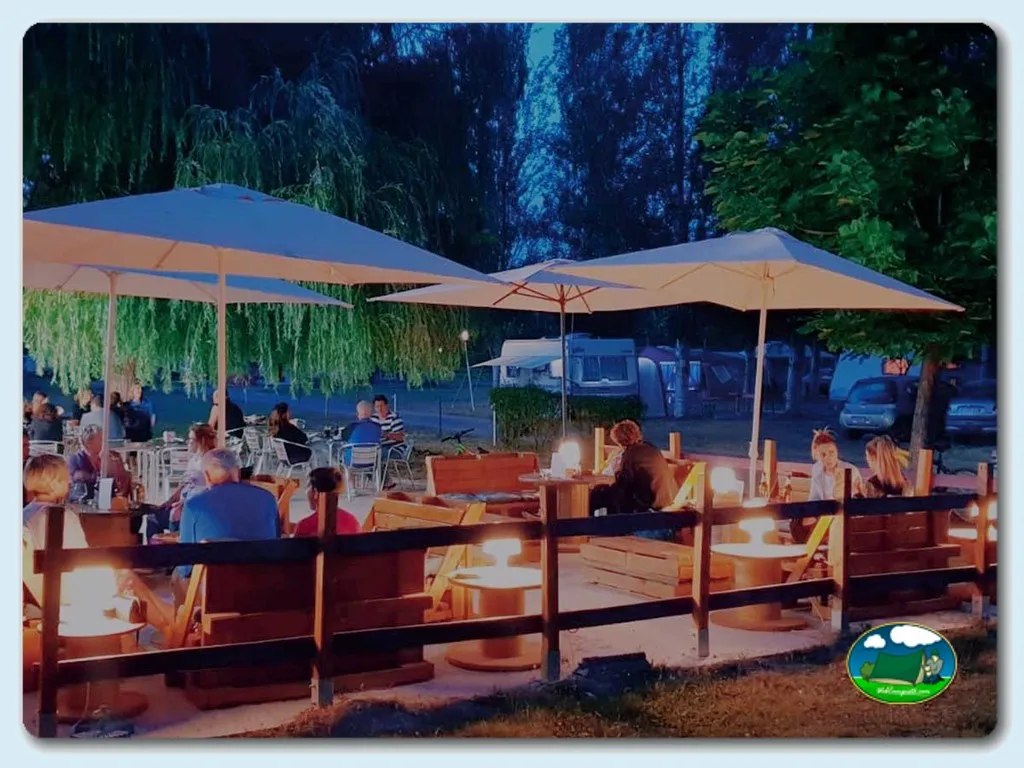 Zona de restaurante junto al río con sombrillas y chimeneas del Camping Camino de Santiago, Villadangos del Paramo (León)