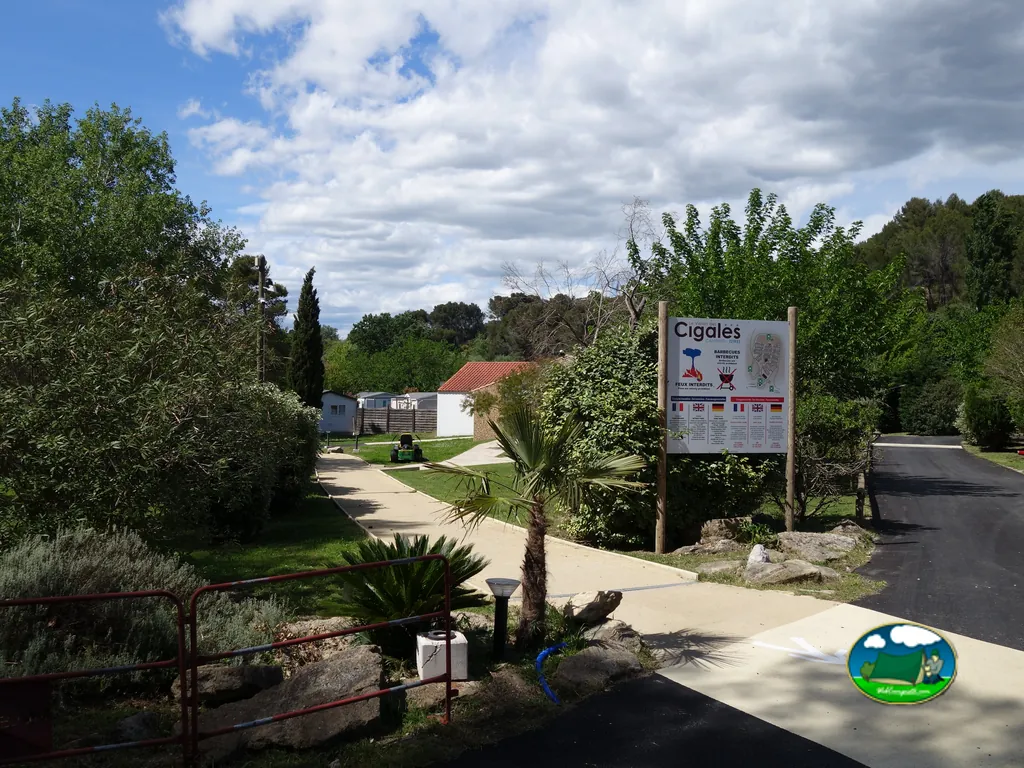 camino de entrada del camping en Istres con cartel de normas y casas móviles entre la vegetación