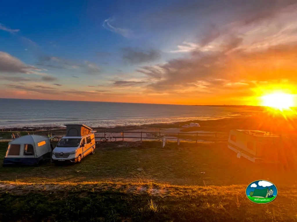 atardecer anaranjado con autocaravana y tienda de campaña acampadas frente al mar