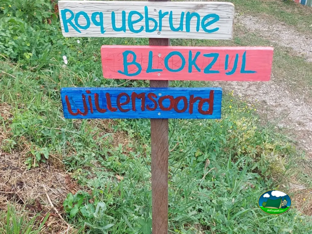 cartel de madera con los nombres de las parcelas pintados a mano entre la hierba