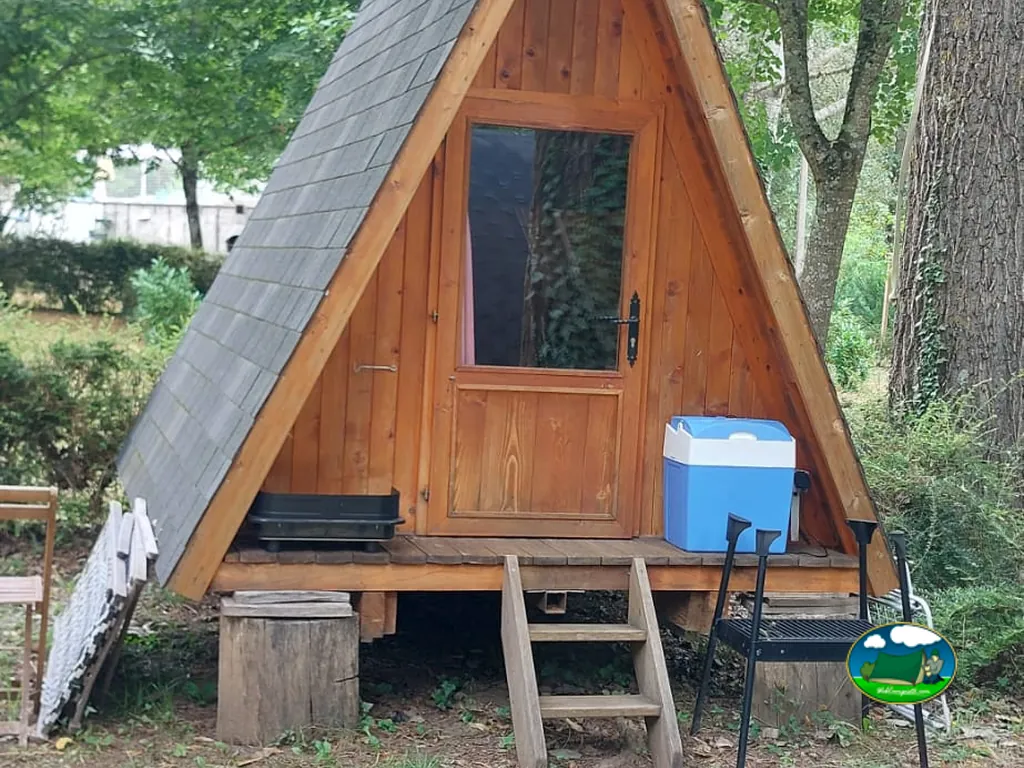 cabaña de madera tipo tienda con nevera portátil y escalones de acceso entre árboles