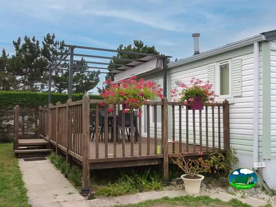 terraza de un mobil-home con pérgola, macetas de flores rojas y mesa exterior
