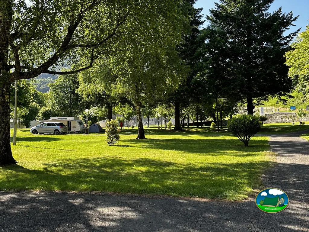parcela de césped arbolada con caravana y coche aparcados en zona de sombra en Sassis