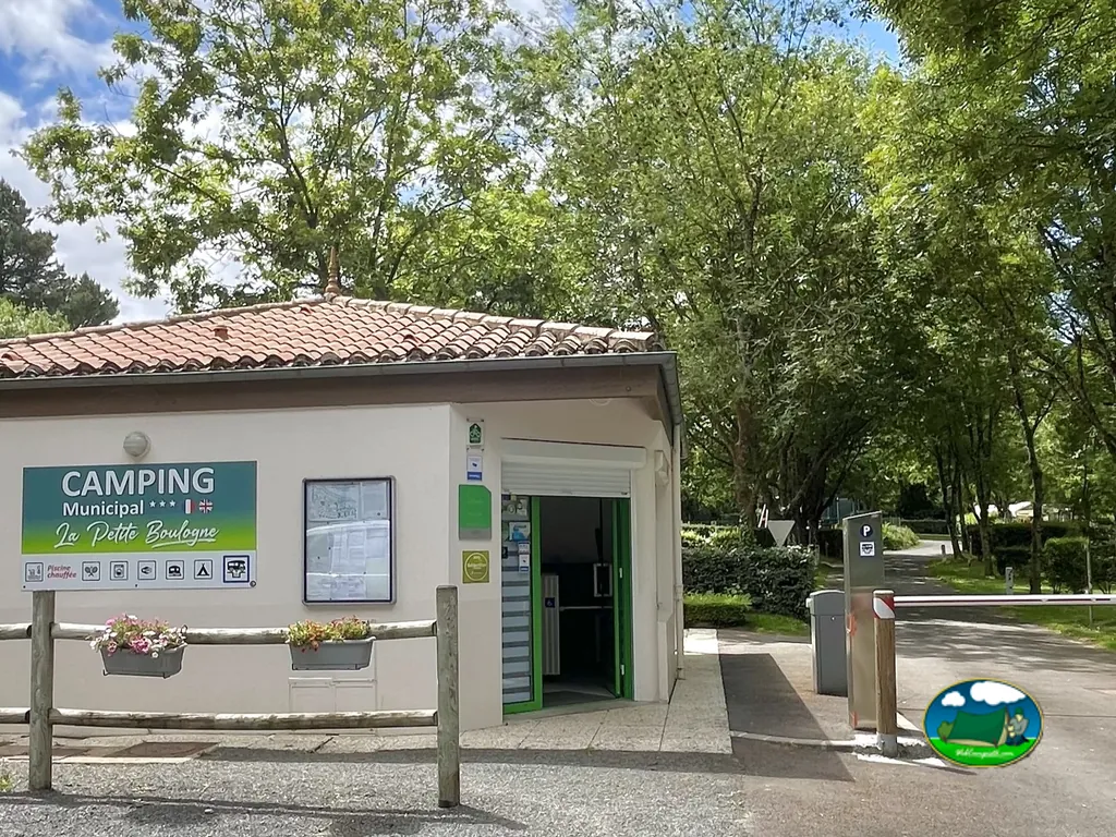fachada de la recepción del camping municipal con barrera de acceso entre los árboles