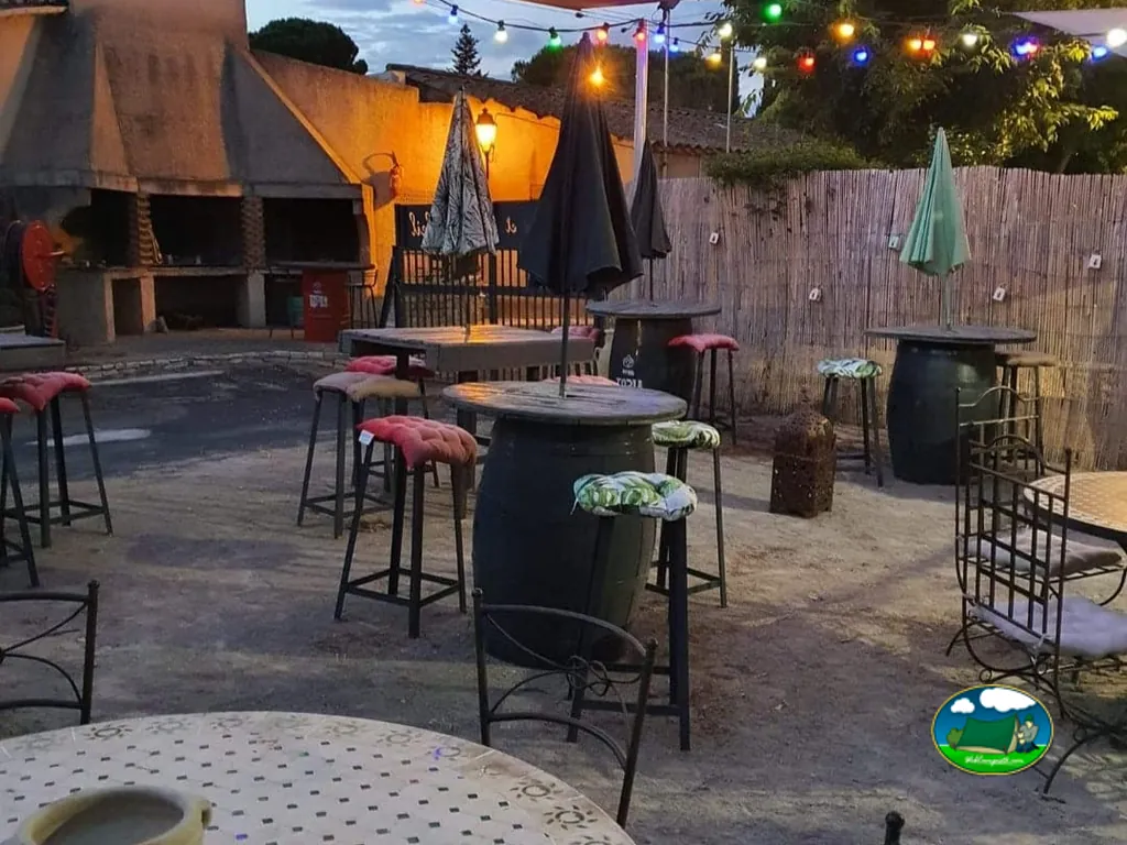 zona de barbacoas y mesas altas con luces de guirnalda al anochecer en el camping de Creissan