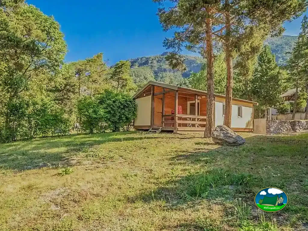 chalet de madera con terraza cubierta y montañas al fondo en Méolans-Revel