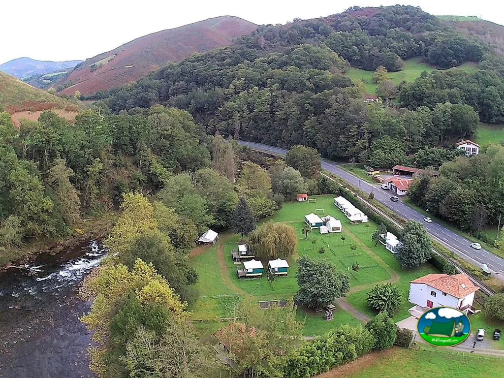 vista aérea del camping junto al río y las montañas de Bidarray, con parcelas y bungalows entre árboles