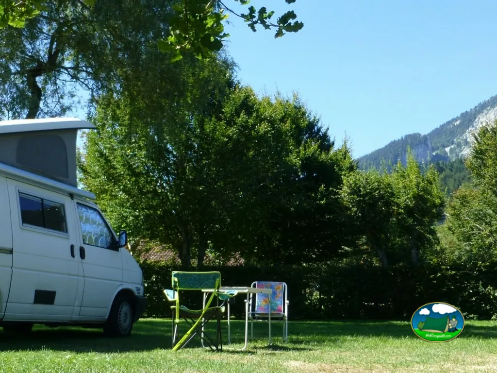 furgoneta camper con mesa y sillas de camping en una parcela arbolada con vistas a la montaña en Saint-Pierre-de-Chartreuse