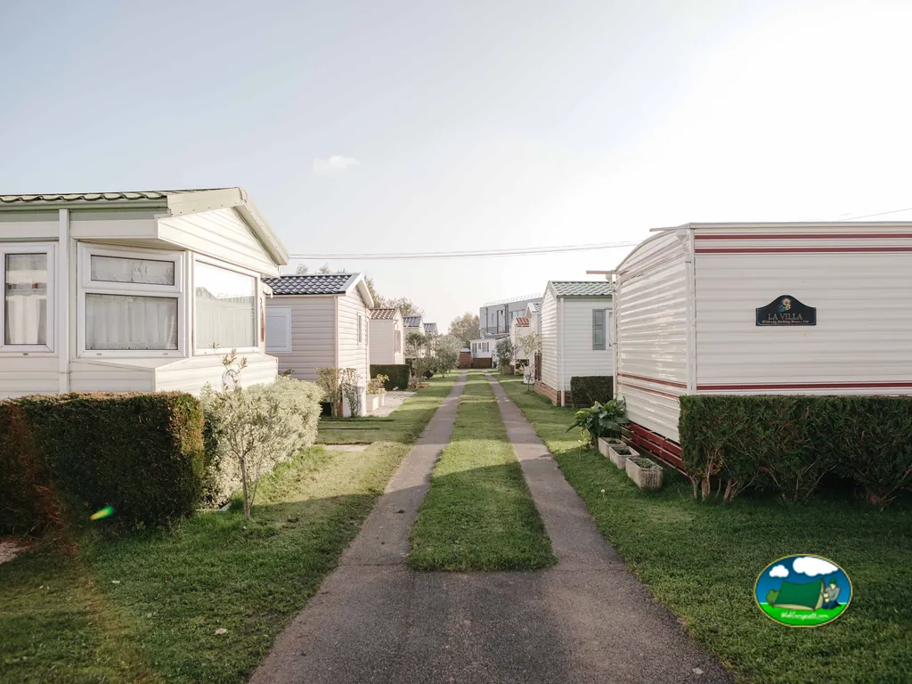 hilera de bungalows con porches junto a un camino ajardinado en el camping de Cabourg