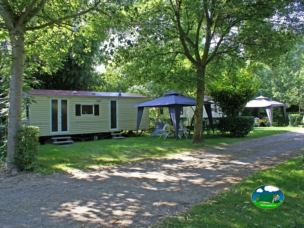 caravana y toldos bajo árboles en las parcelas del camping des Grottes en Perrier