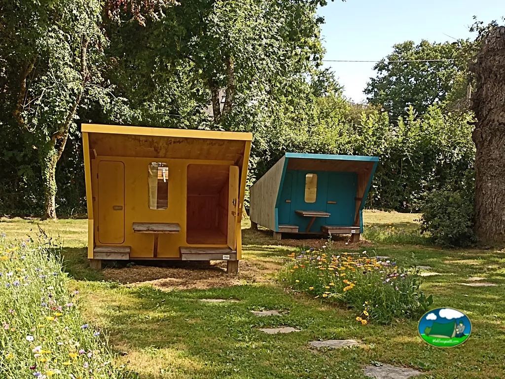 dos cabañas infantiles de madera pintadas de amarillo y azul entre flores silvestres en Arradon