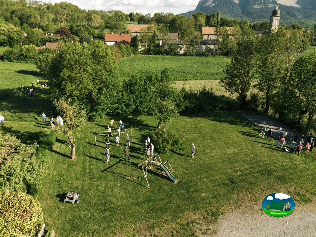 vista aérea de la zona de juegos y voleibol del camping con el pueblo y la montaña al fondo en Aubessagne