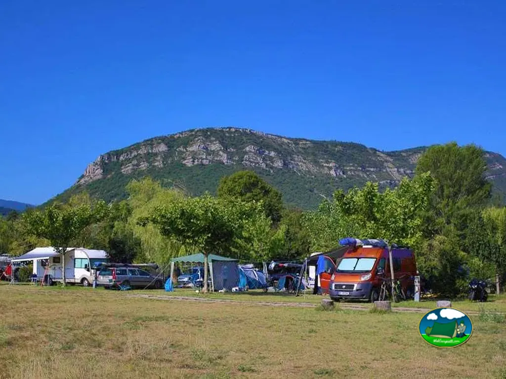 parcelas con autocaravanas bajo árboles frente a un macizo rocoso en Laragne-Montéglin