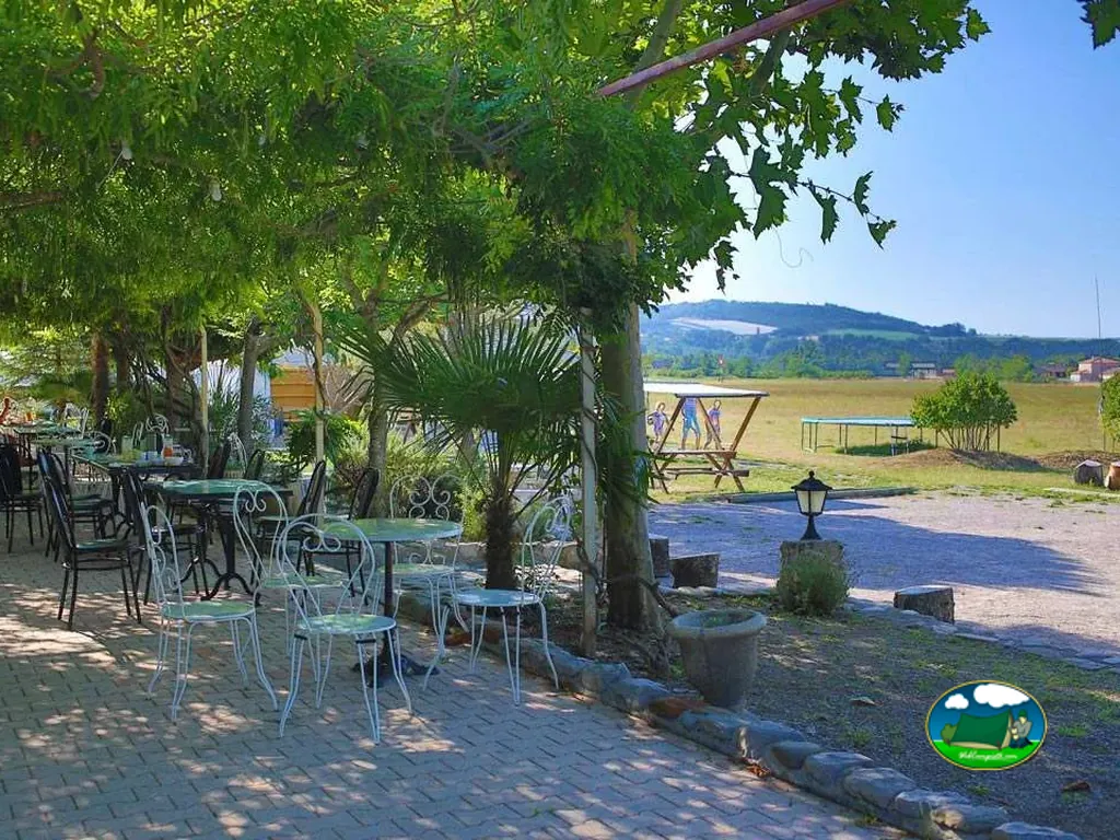 terraza con mesas y sillas de hierro bajo una enredadera junto a una zona de juegos y colinas al fondo en Laragne-Montéglin