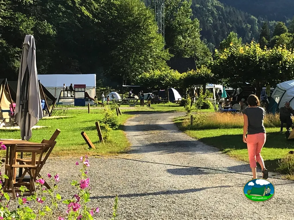 camino de grava entre tiendas y caravanas bajo montañas boscosas con una persona caminando de espaldas