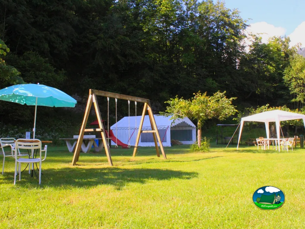 zona infantil con columpios, tobogán y carpas blancas junto a césped y bosque