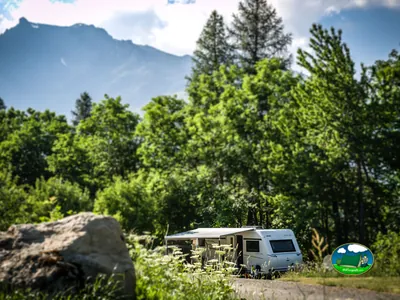 caravana aparcada en una parcela junto a un bosque de montaña con flores silvestres en primer plano