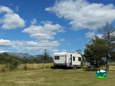 caravana en una parcela de césped con mesas y sillas bajo un cielo nuboso y montañas en Castellane