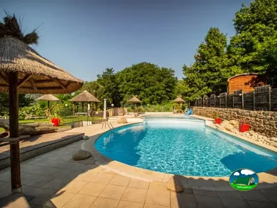 piscina con sombrillas de paja y bungalows alrededor en un jardín arbolado en Ribes
