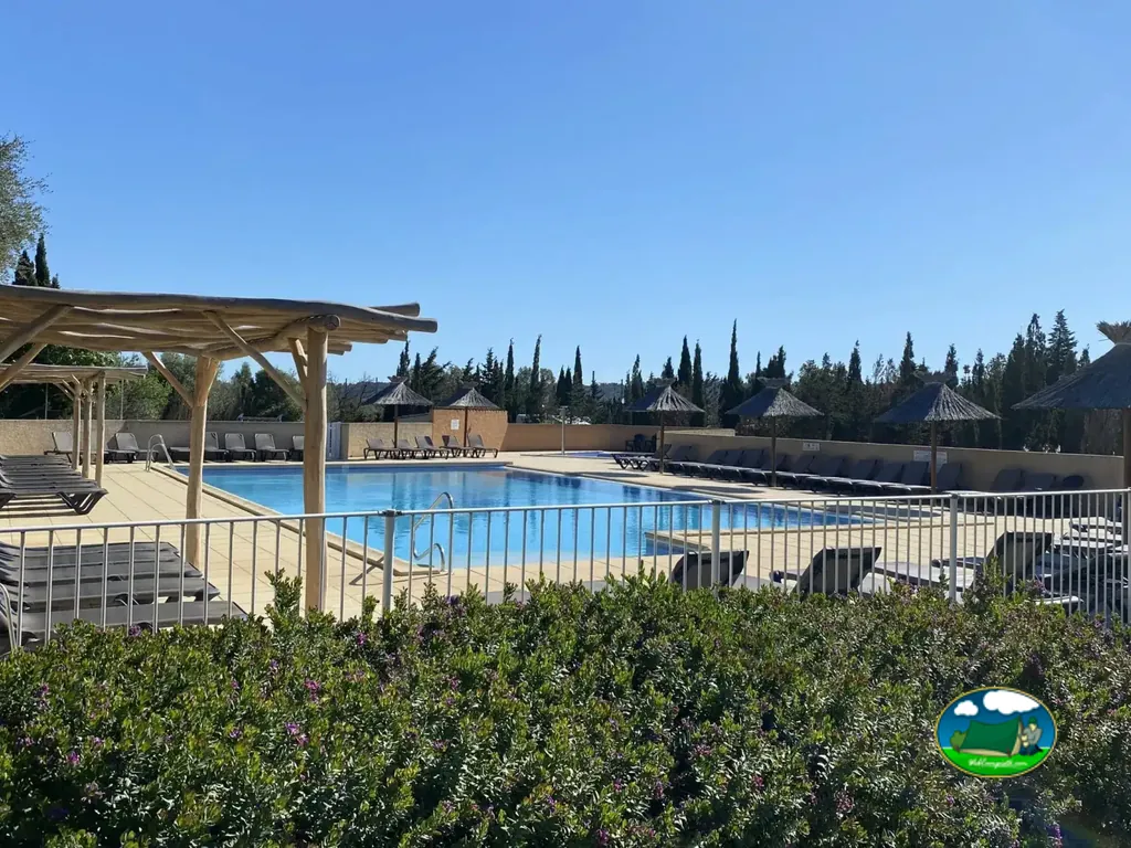 piscina con pérgola de madera y sombrillas de paja rodeada de tumbonas en Fitou