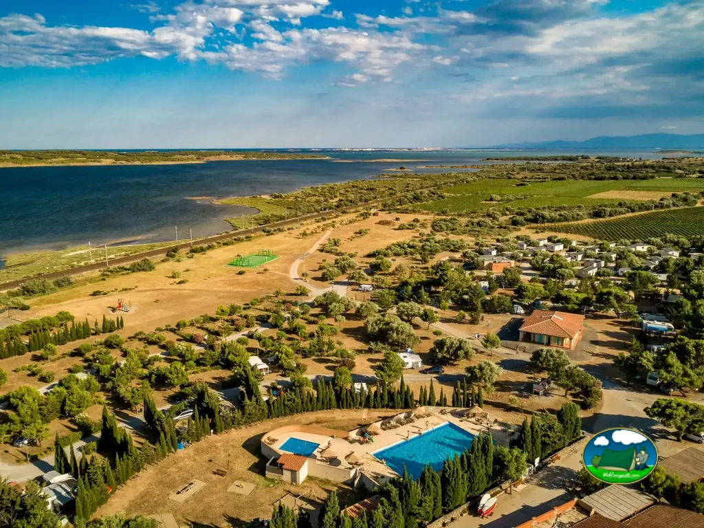 vista aérea del camping junto a una laguna con bungalows, piscinas y parcelas arboladas en Fitou