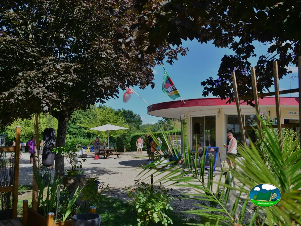 edificio de recepción con banderas junto a una terraza con mesas y varias personas alrededor