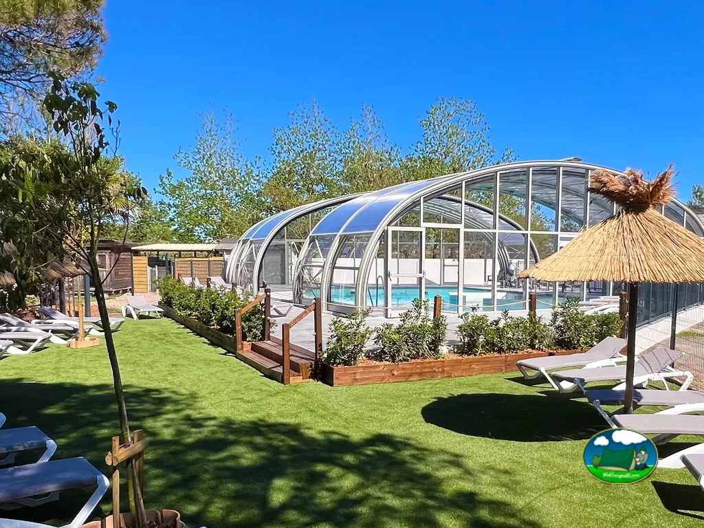 piscina climatizada con cúpula retráctil y tumbonas bajo sombrilla de paja en Vias