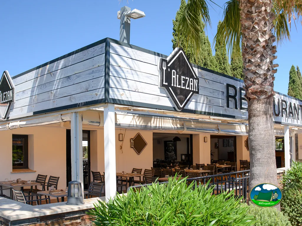 terraza del restaurante L'Alezan del camping con mesas junto a una palmera