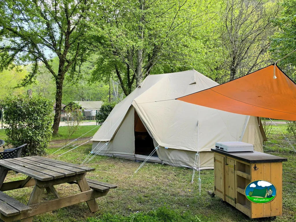 tienda de campaña tipo glamping con cocina exterior de madera y mesa de picnic