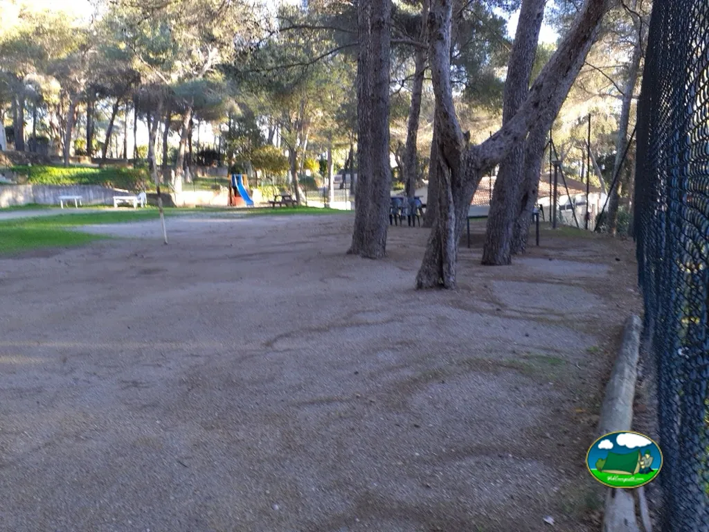 parcela de acampada de tierra bajo pinos con un tobogán infantil al fondo en La Croix-Valmer