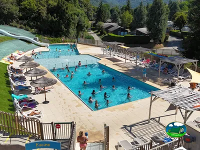 piscina concurrida con tobogán y bañistas vista desde arriba, chalets entre montañas boscosas en Saint-Geniez-d'Olt