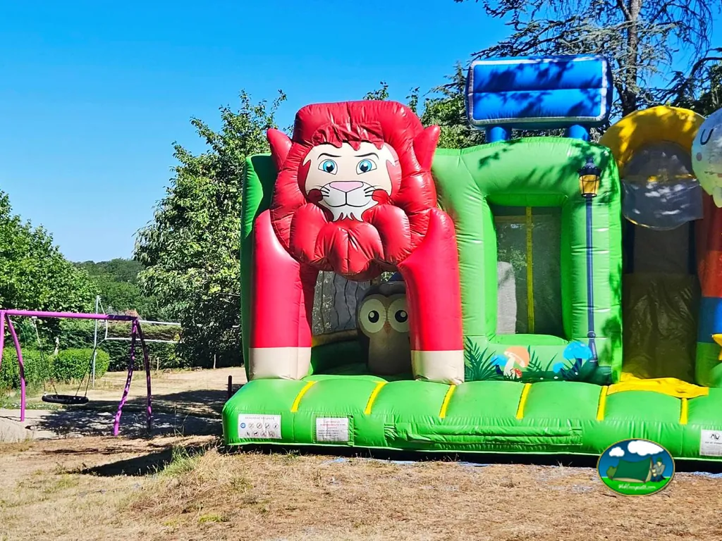 tobogán hinchable infantil con forma de león junto a columpios en una zona de césped