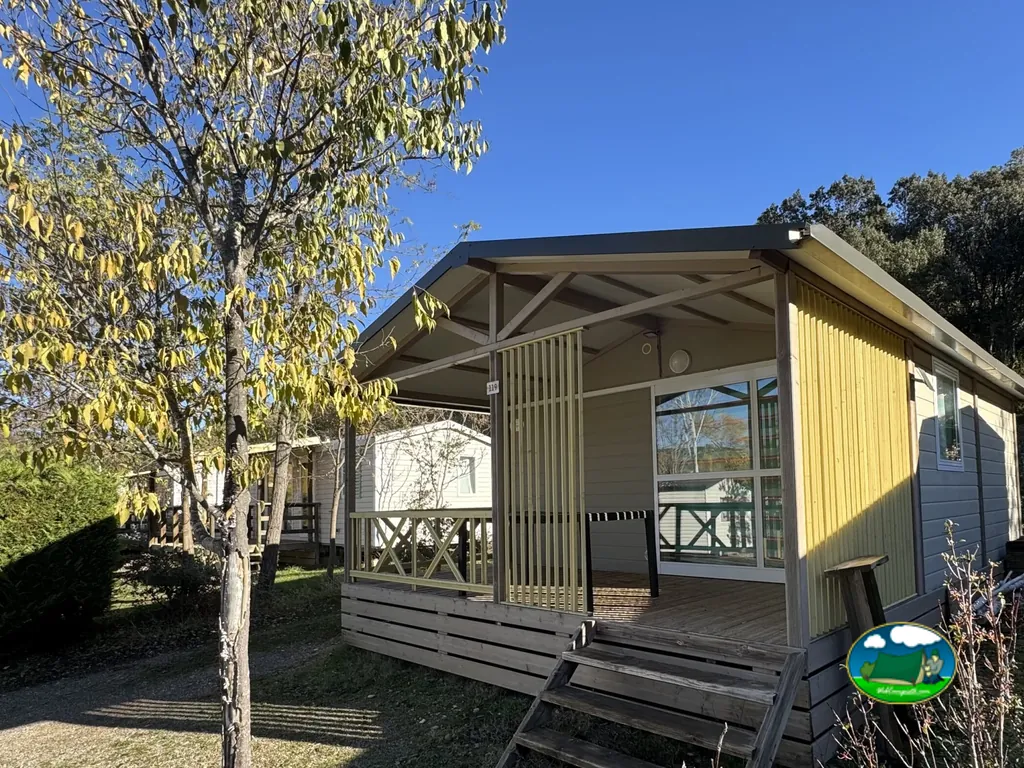 bungaló con revestimiento amarillo y porche cubierto entre árboles de otoño