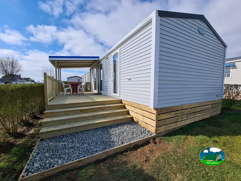 mobil-home blanco con terraza cubierta, mesa y sillas en Saint-Jouin-Bruneval